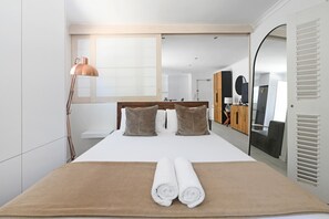 Une chambre d’hôtel moderne avec un grand lit, une tête de lit en bois, une grande fenêtre, un miroir et une armoire.