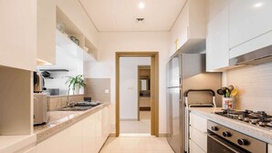 A modern kitchen with white cabinetry, a stainless steel refrigerator, a gas stove, and a microwave. - StayShort - 2 Bed in Downtown Dubai that Sleeps 4 with Canal Views! (Downtown)