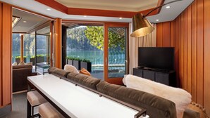 Una sala moderna con sofá, una mesa de comedor y televisor. Se aprecia una ventana grande con vistas a un lago y árboles.