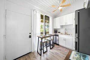 A compact kitchen with a wooden table, two bar stools, a refrigerator, and a ceiling fan. - Bright North Shore Condo With Loft, Golf Views, and Resort Amenities (Kahuku)