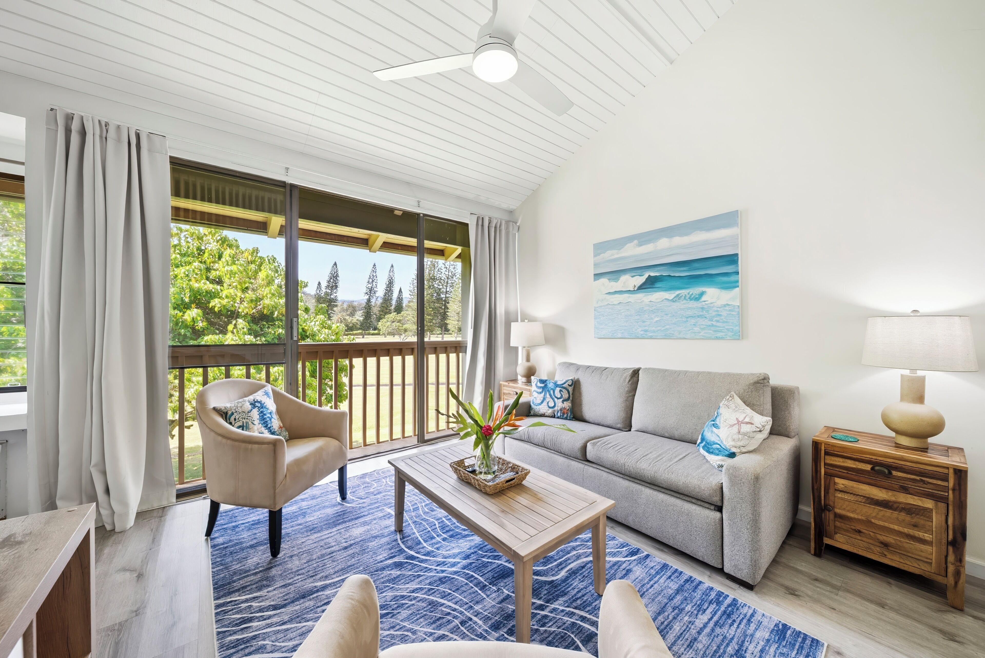 A living room with a sofa, armchair, coffee table, and a painting of a beach scene.