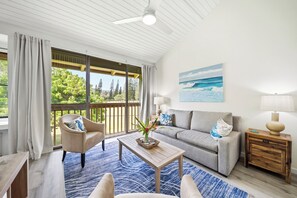 Un salon comprenant un canapé, un fauteuil, une table basse et un tableau représentant une scène de plage.