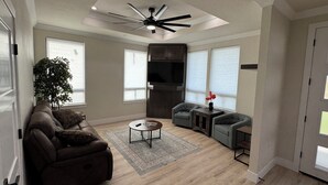 A spacious living room with a ceiling fan, a large window, a dark entertainment unit, and a grey sofa. - Fabulous 2-bedroom house with private boat ramp access to the Sacramento River (Redding)