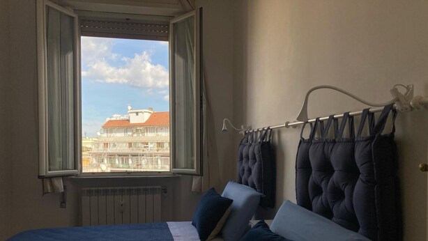 A bedroom with two beds, a window with curtains, a radiator, and a view of buildings outside. - Apartment with panoramic view - Holiday Home Giulia (Roma)