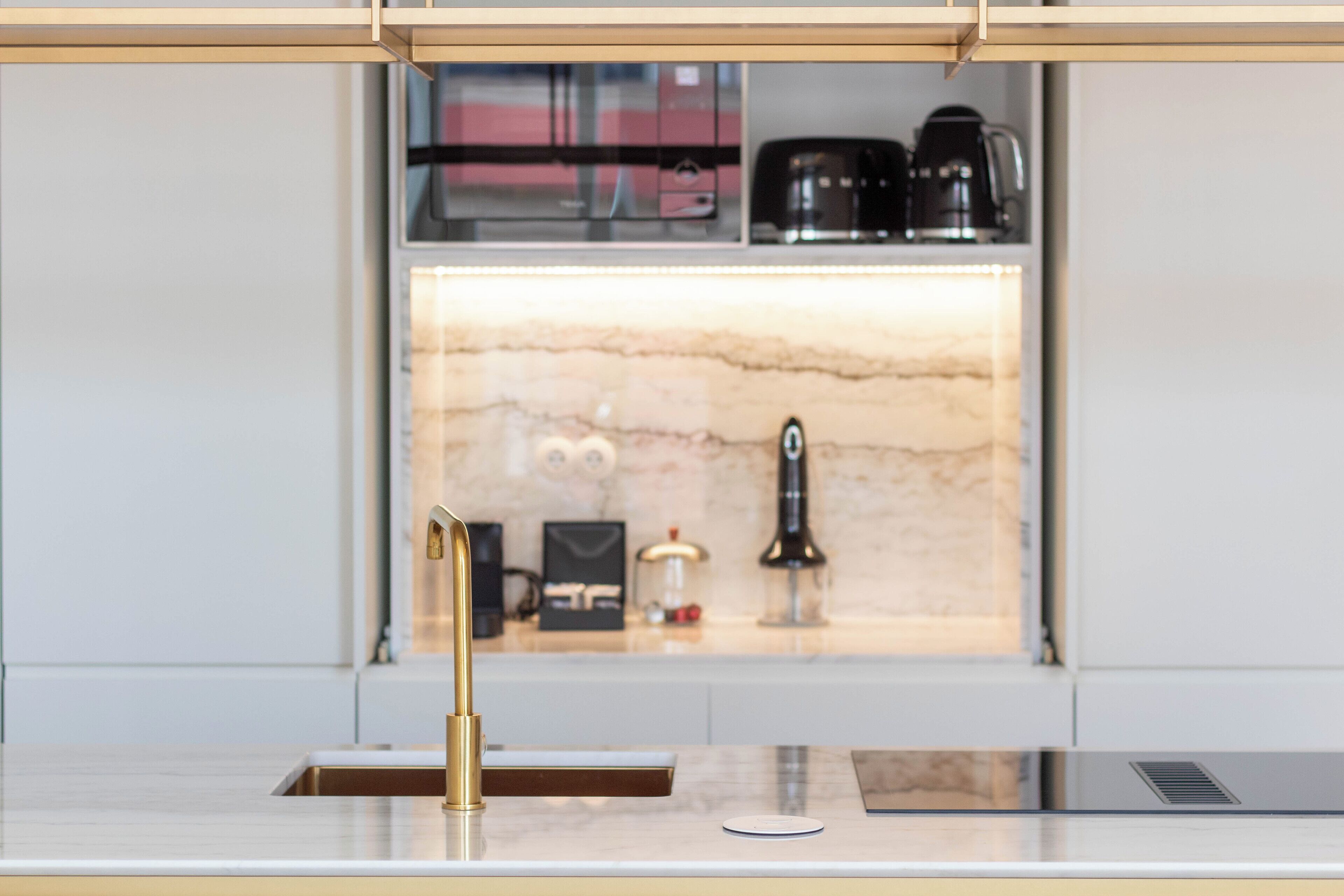 A modern kitchen with a marble backsplash, a gold faucet, and a coffee machine on the counter.