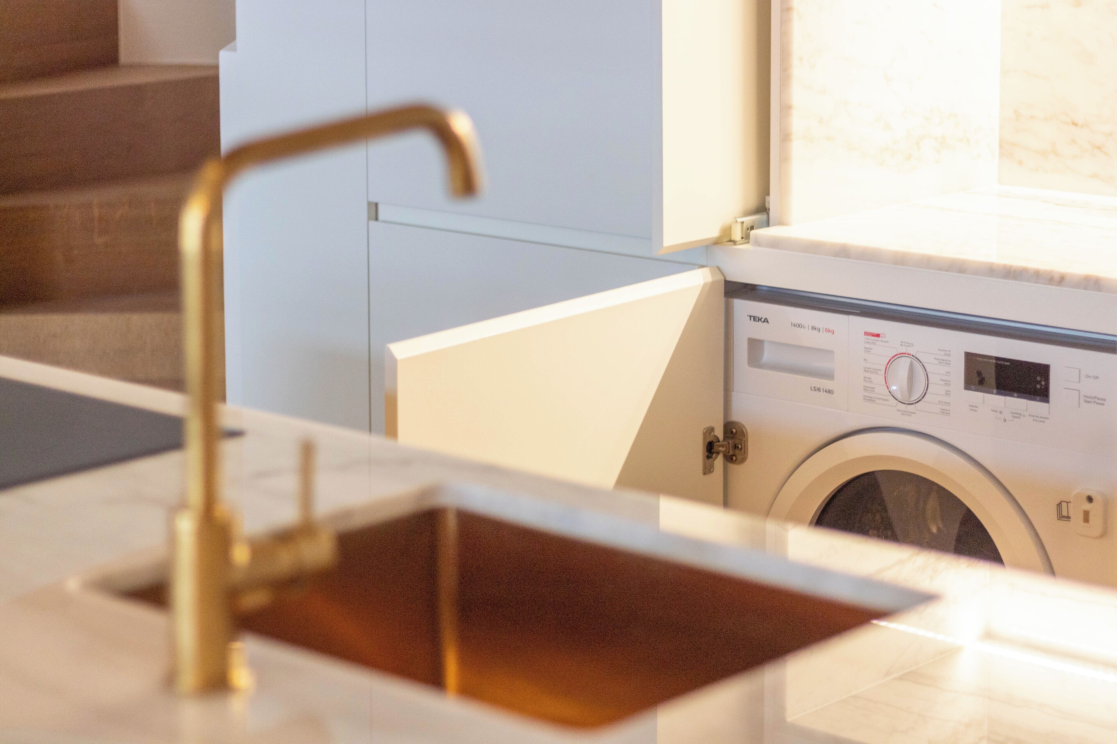 Een moderne badkamer met een gouden kraan, een ingebouwd wastafelmeubel en een wasmachine.