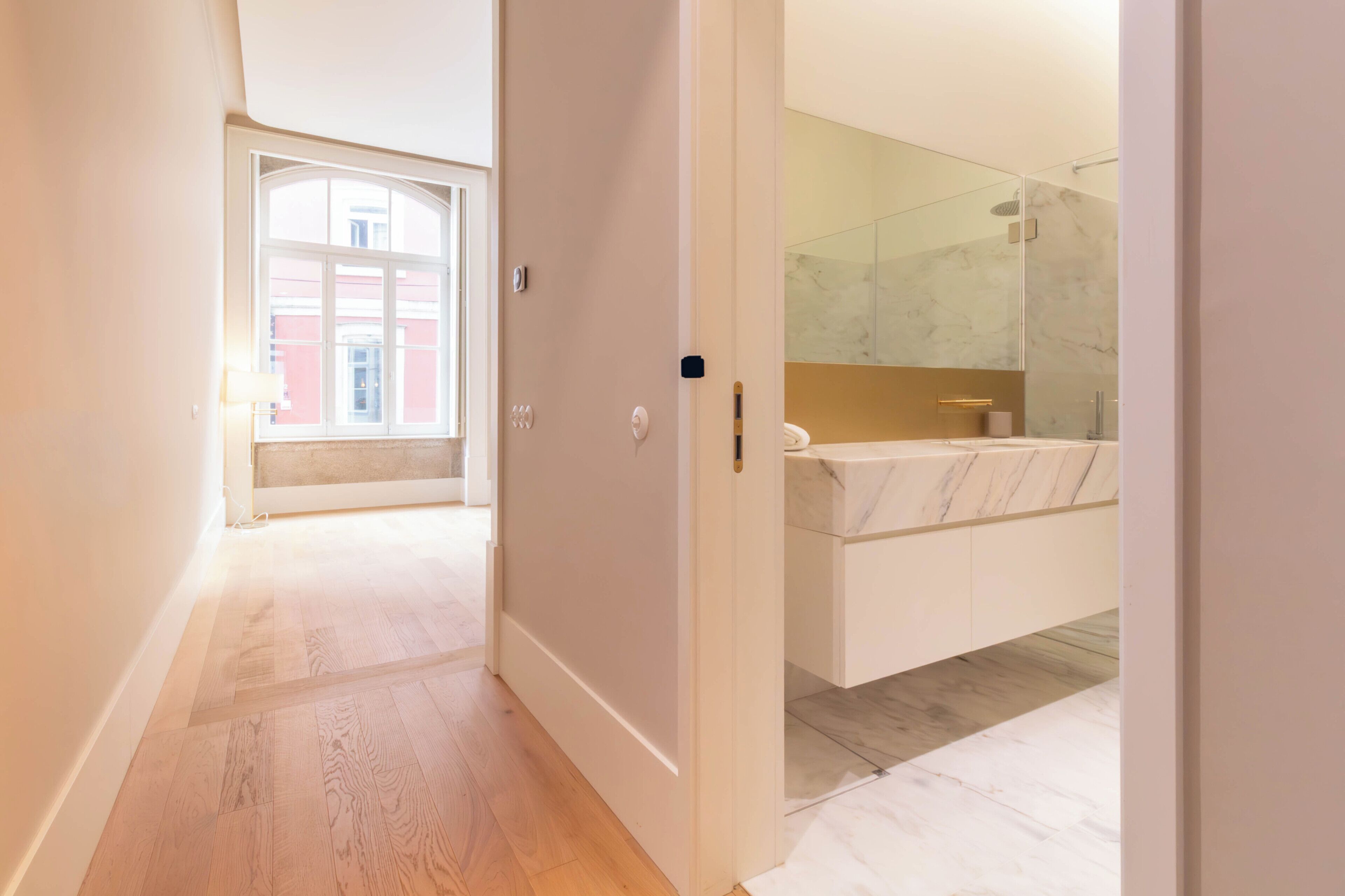 Un couloir mène à une salle de bain dotée d’un lavabo en marbre et d’une cabine de douche en verre.