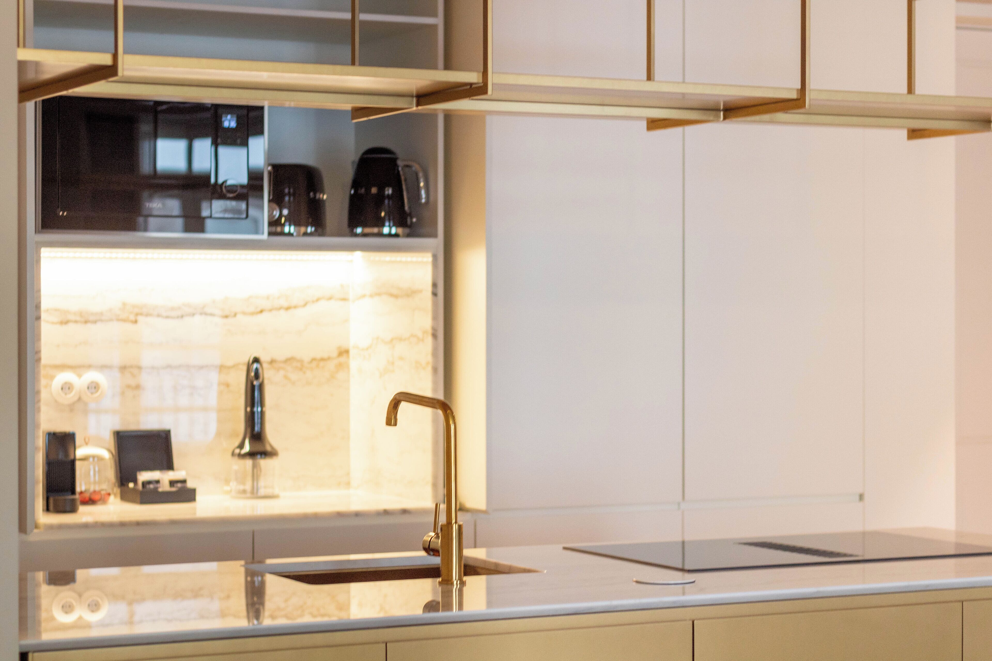 Eine moderne Küche mit Marmorarbeitsplatte, einem goldenen Wasserhahn und einer Kaffeemaschine im Regal.