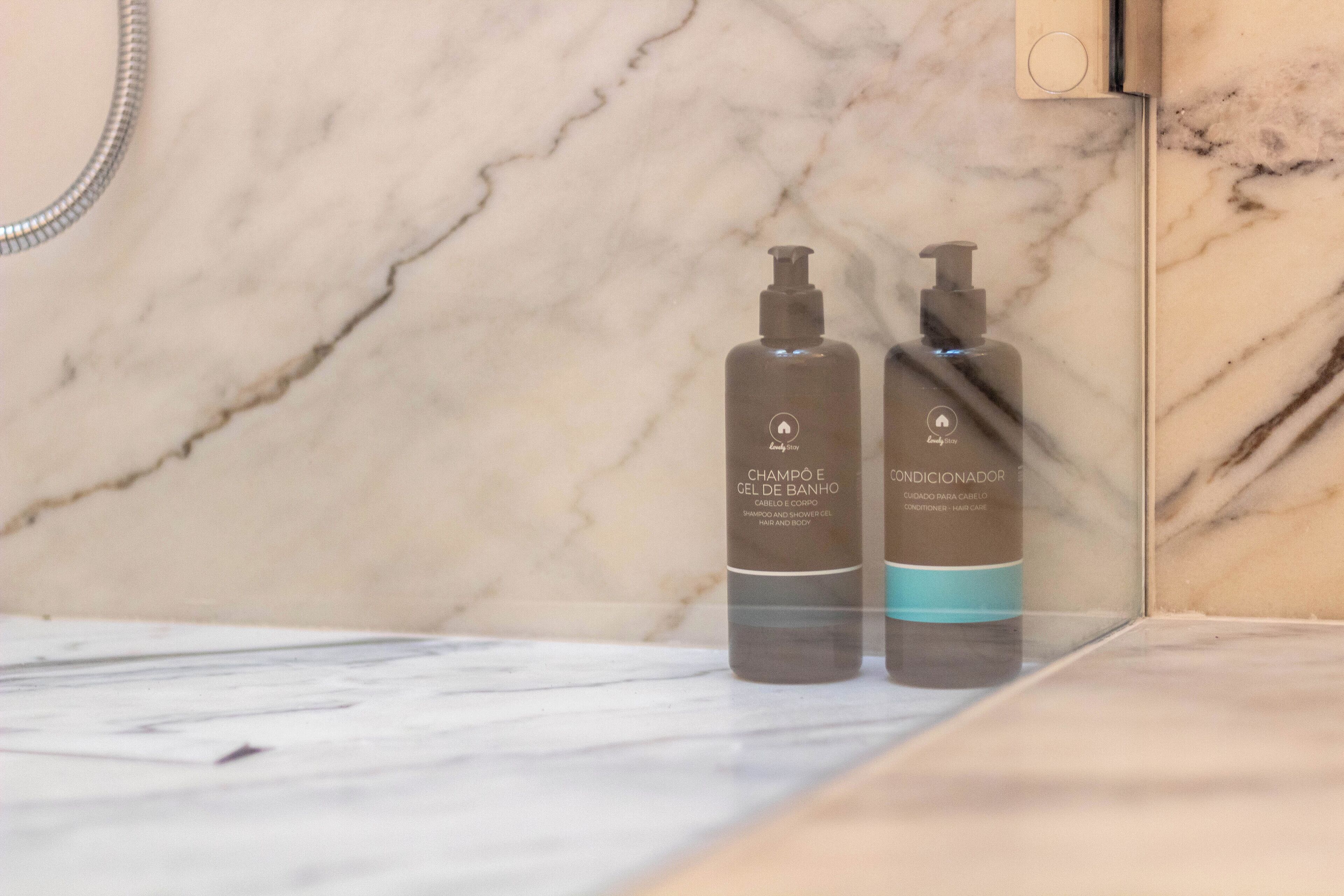 Dois frascos de shampoo e condicionador sobre uma bancada de mármore em um banheiro.
