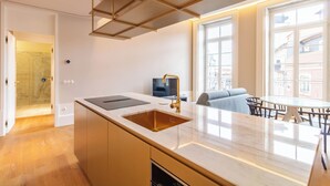 A modern kitchen with a large island, a built-in oven, and a sink. There is a dining area with a glass table and chairs. - Entreparedes House (Porto)