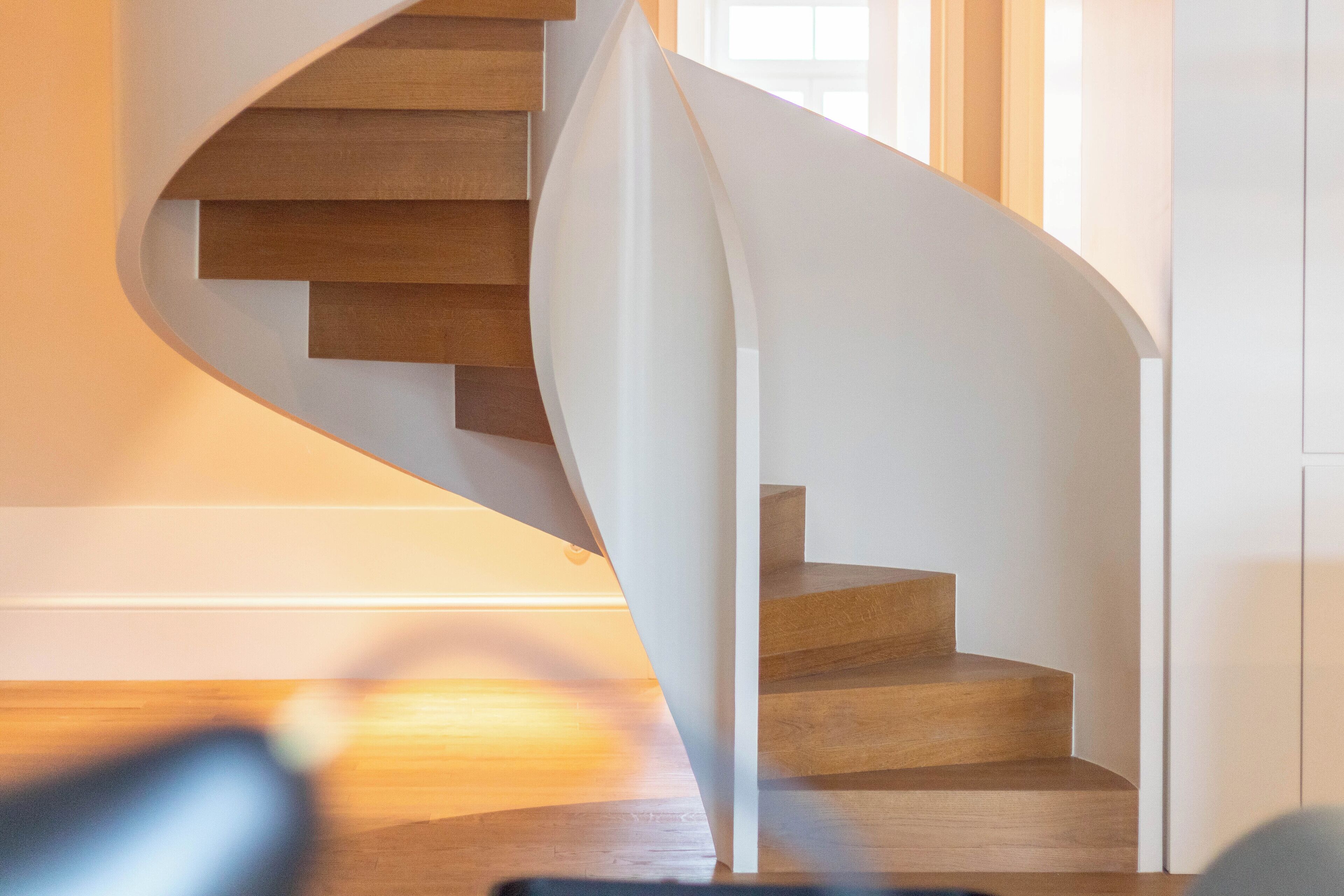 A spiral staircase with wooden steps and white walls, leading to an upper floor.