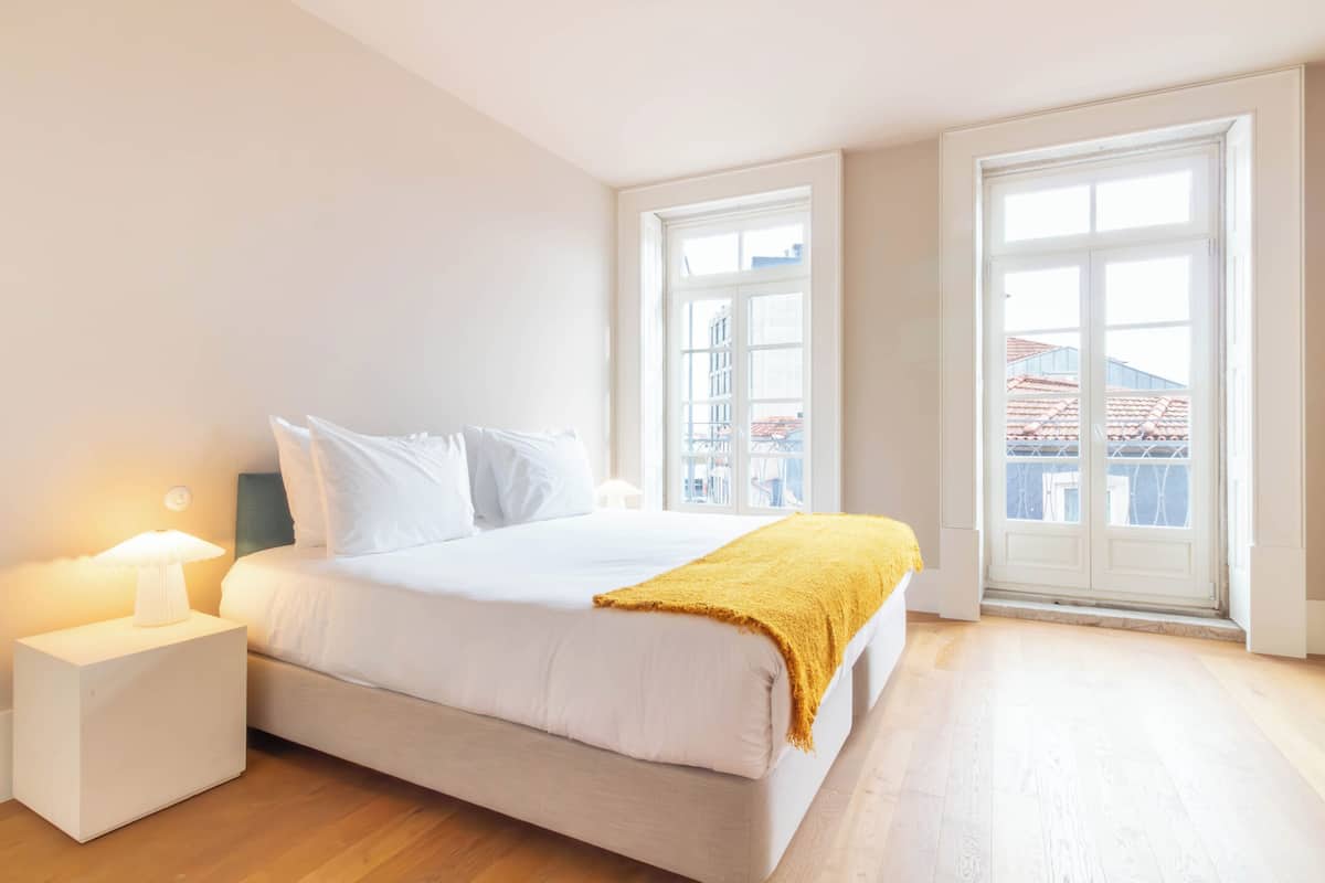 Une chambre à coucher avec un lit, une table de chevet, une lampe et de grandes fenêtres.