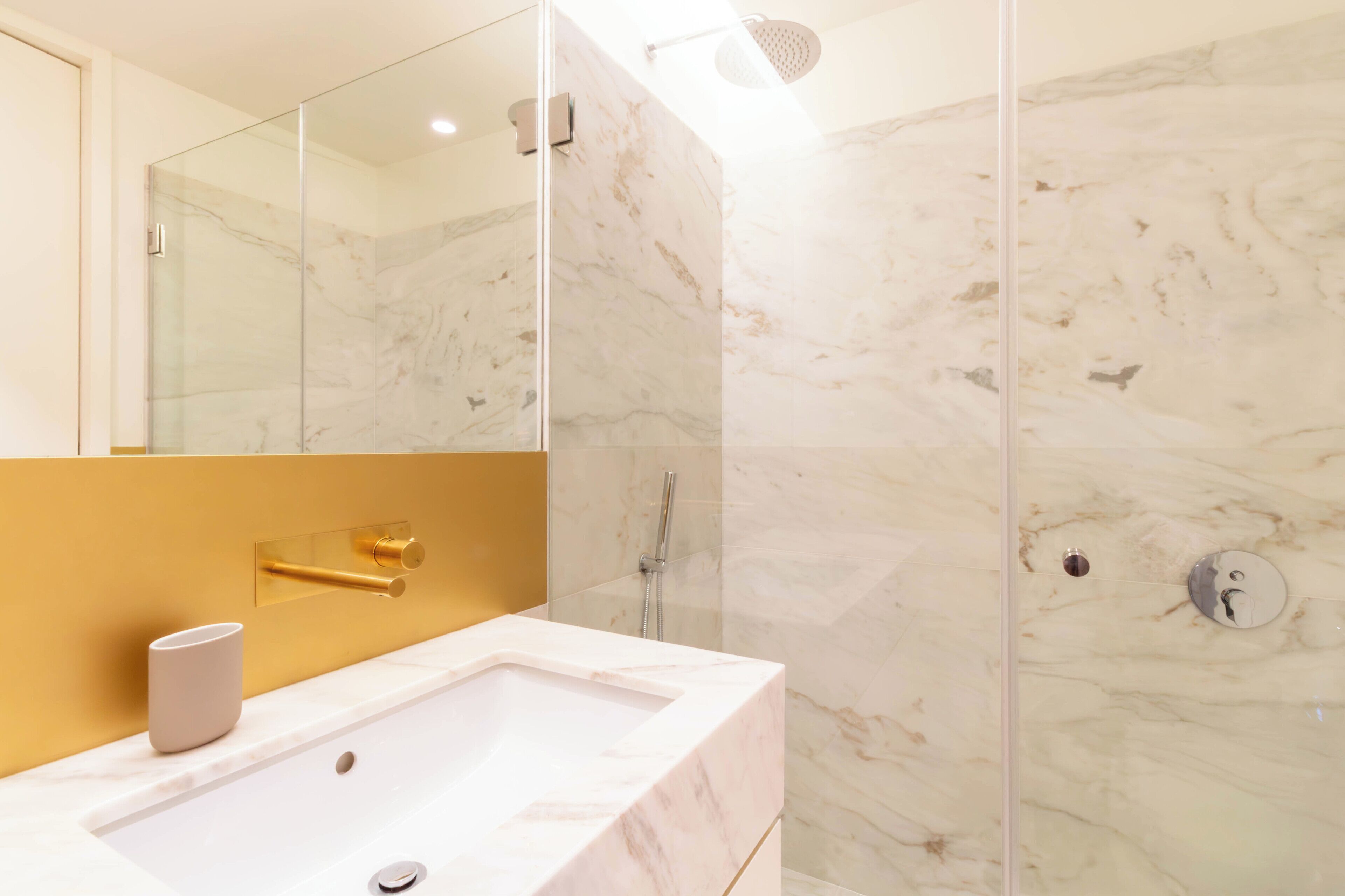 A modern bathroom with a marble sink, a glass-enclosed shower, and a gold-colored wall.