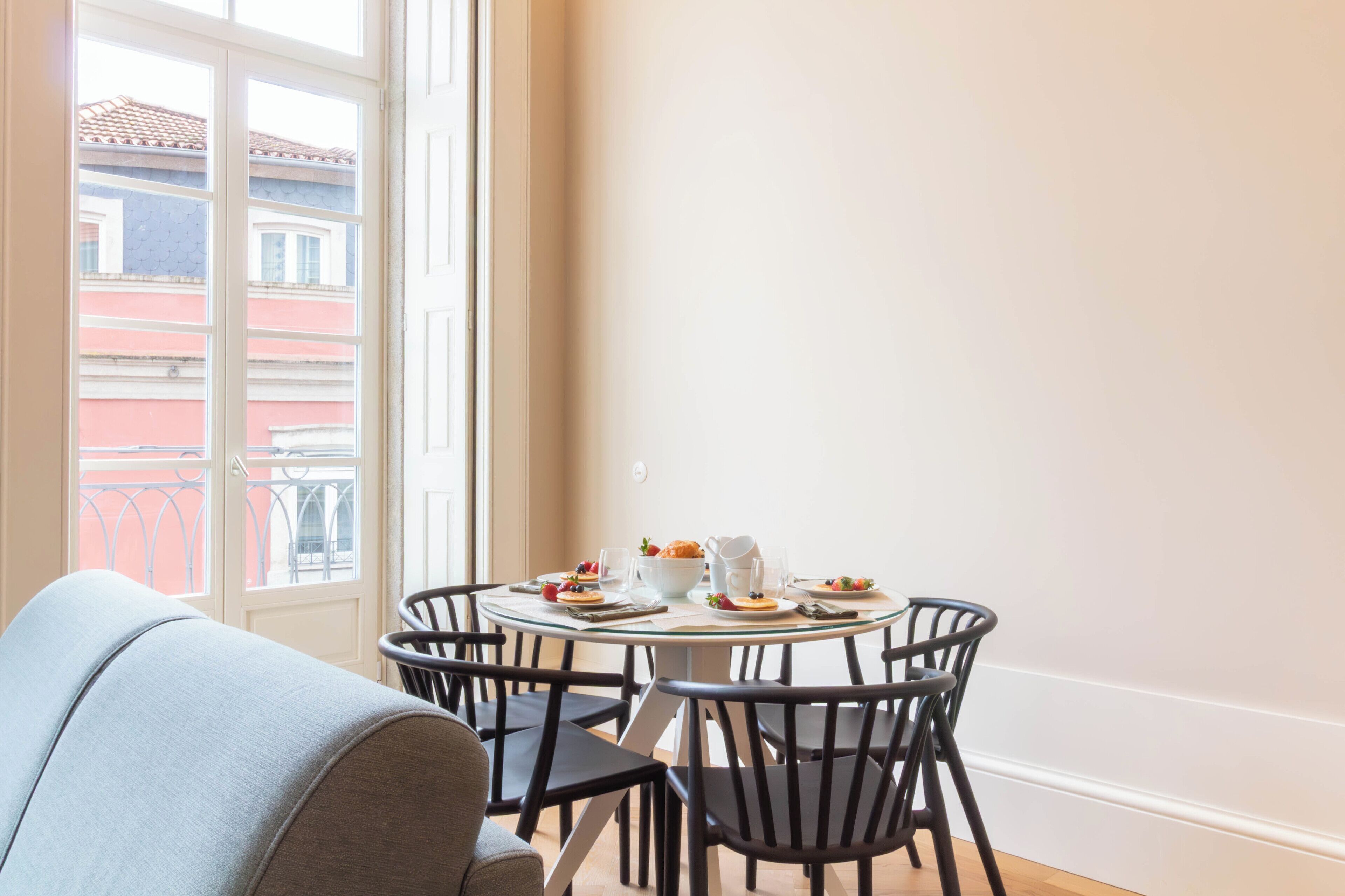 A dining area with a round table set for four, surrounded by black chairs. A white sofa is positioned in the foreground.