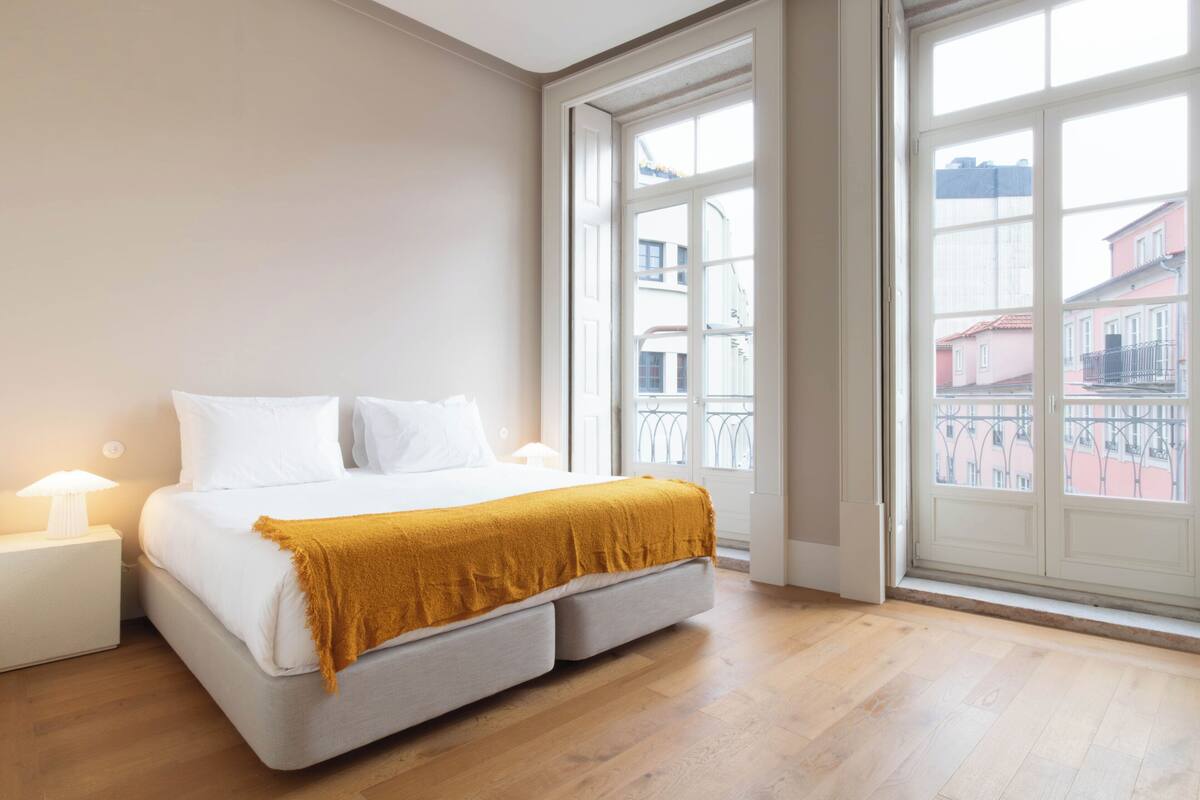Une chambre à coucher avec un lit, des tables de chevet, une fenêtre et une vue sur des immeubles.
