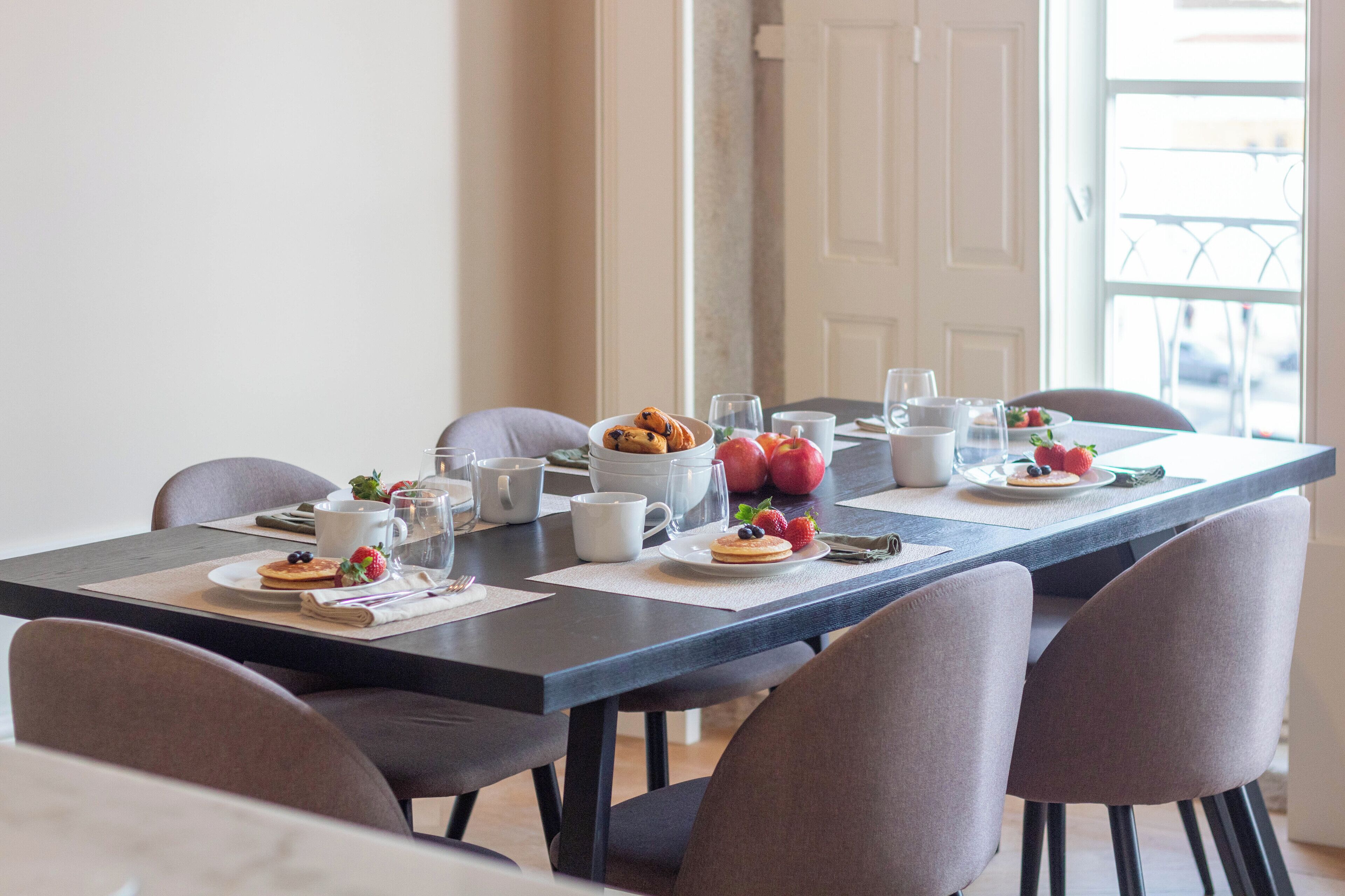 A dining table set with breakfast items, including pancakes, fruits, and cups.