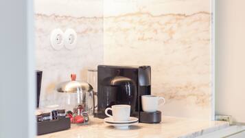 A modern kitchen with a marble countertop, a coffee maker, a cup, and a kettle.