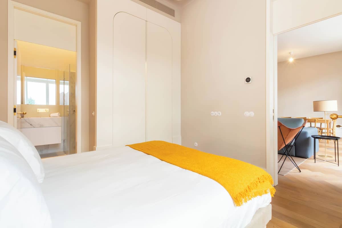 Une chambre d’hôtel comprenant un lit, une salle de bain avec un miroir et un coin salon avec une table et des chaises.