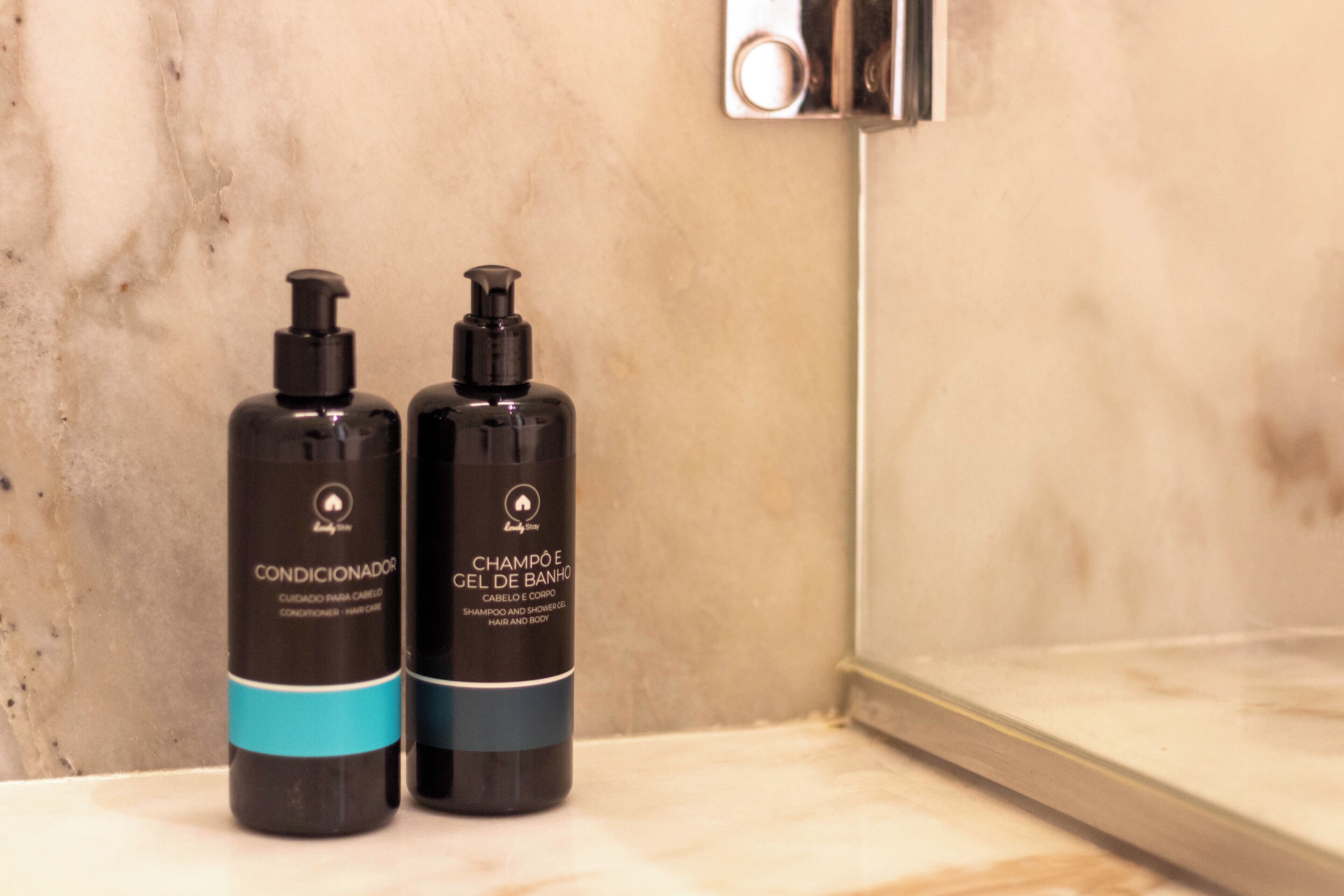 Dos botellas negras de productos para el cabello sobre una encimera de mármol en un baño.