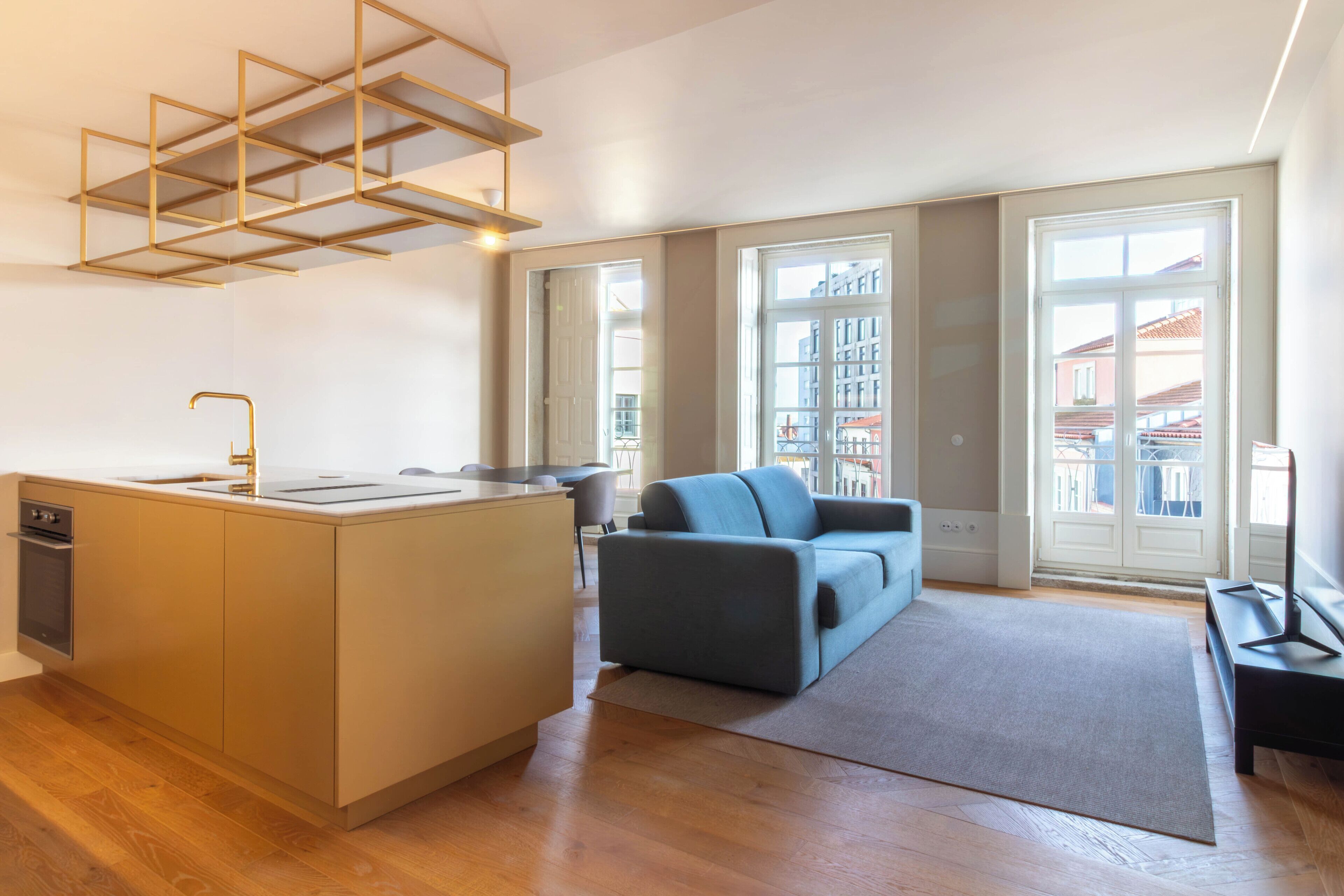 A modern apartment with a kitchen island, a sofa, and large windows offering a view of buildings.