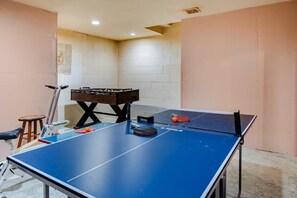 Een kamer met een blauwe tafeltennistafel, een tafelvoetbaltafel en een klein krukje.