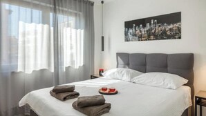 A hotel room with a bed, a cityscape painting, and a window with sheer curtains. - Apartment Citylight | Belvedere Holidays – Sea Views & Modern Comfort (Novigrad)