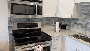 A kitchen with white cabinets, a microwave, an oven, a stove, and a tiled backsplash. - Across the street from Indian Shores Beach Condo (Indian Shores)
