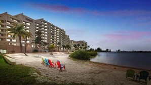 Ett hotell vid stranden med flera våningar, palmer och en sandstrand med färgglada stolar.