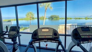 Ett gym med löpband och utsikt över en sjö eller annat vattendrag omgivet av träd.
