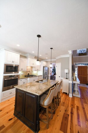 A modern kitchen with white cabinetry, stainless steel appliances, a granite countertop, and a central island with bar stools. - 8 bedroom home in Evans with pool - 1.5 miles from ANWA , 13 miles to Masters! (Evans)