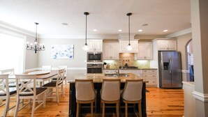 Une cuisine moderne avec des meubles blancs, un réfrigérateur en acier inoxydable et un coin bar équipé de tabourets.