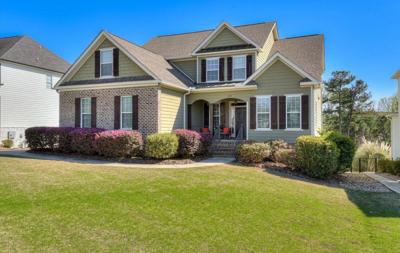 A two-story house with a front porch, brick facade, and a well-maintained lawn.