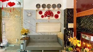 Un salon moderne avec un canapé gris, un mur décoratif orné d’horloges indiquant le nom de différentes villes, et une petite table sur laquelle sont posés un appareil photo et des fleurs.