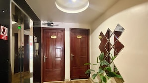 Un couloir avec deux portes en bois portant les numéros 001 et 002, une plante en pot et un miroir décoratif fixé au mur.