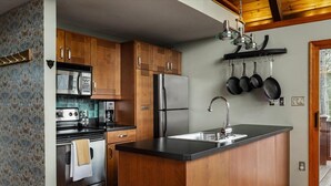 A kitchen with wooden cabinets, stainless steel appliances, and a black countertop island. - Moon View A-Frame - Wood Sauna, Mountain Views, Fire Pit, Wood Stove, Stargazing (Lost River)
