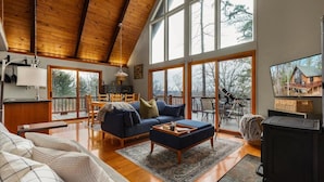 A spacious living room with a high ceiling, large windows, a fireplace, and a cozy seating area. - Moon View A-Frame - Wood Sauna, Mountain Views, Fire Pit, Wood Stove, Stargazing (Lost River)