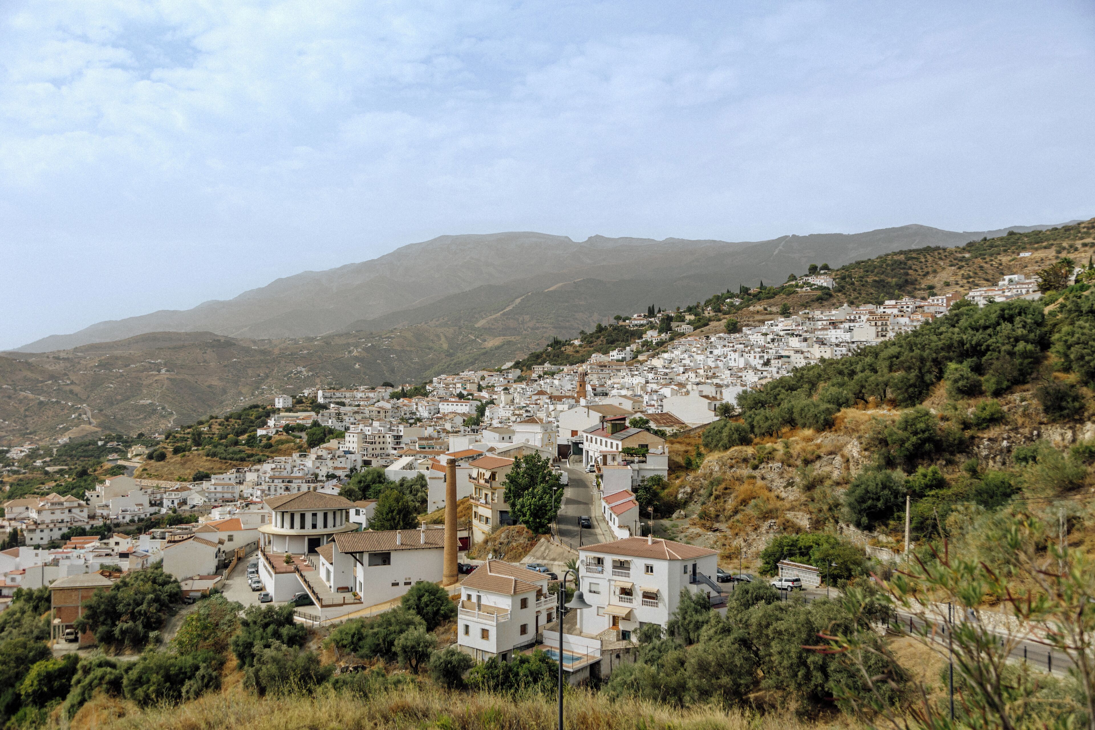 Une ville perchée sur une colline, avec des bâtiments blancs, une église imposante et une chaîne de montagnes en arrière-plan.