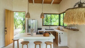 Cozinha moderna com ilha central, banquetas de madeira, luminárias pendentes e vista para o verde lá fora.