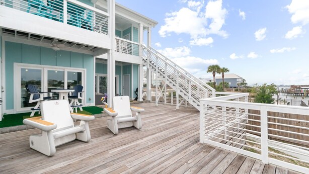 Une terrasse en bois avec deux chaises longues blanches, un escalier menant à un deuxième niveau et une vue sur l’océan.