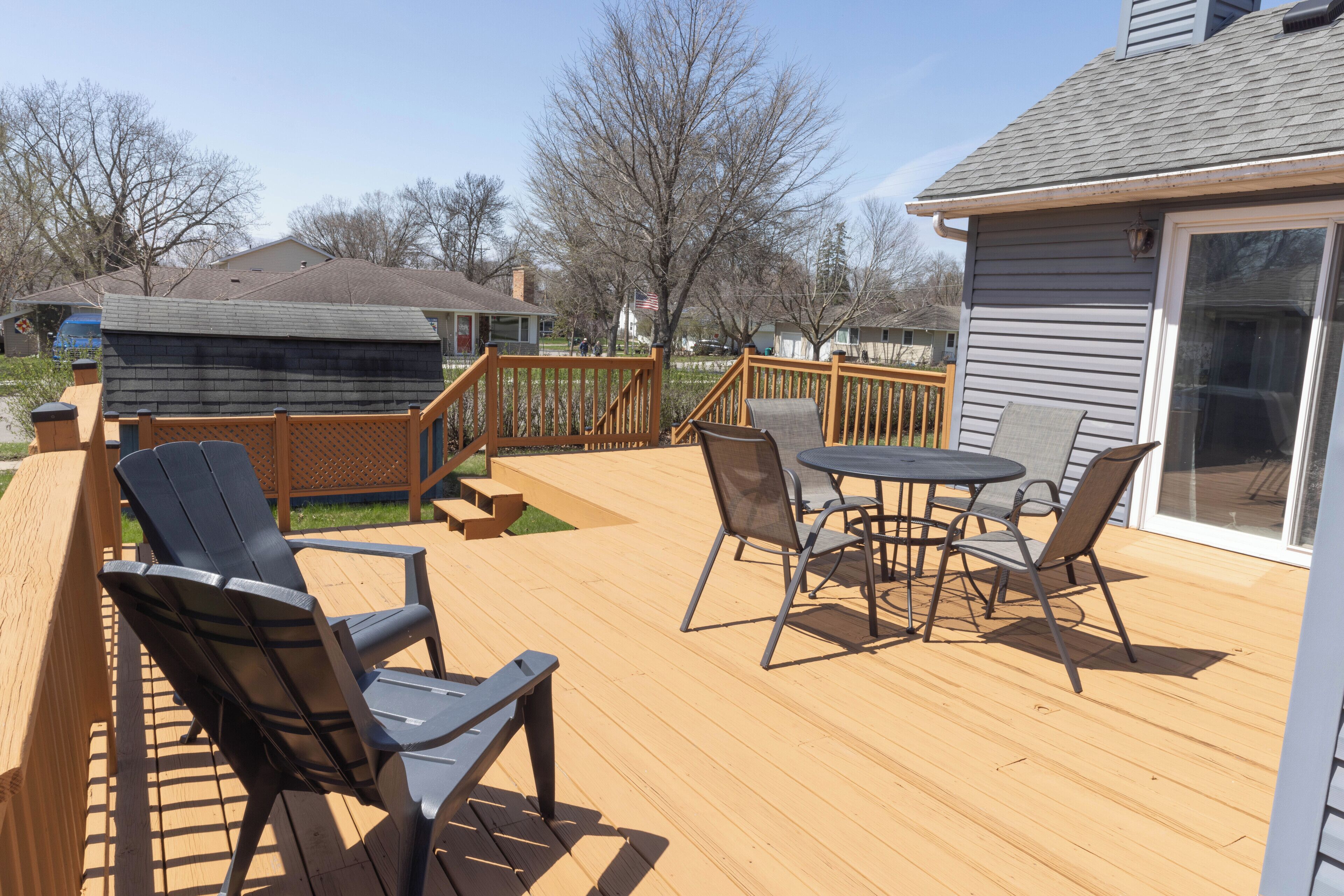 A wooden deck with outdoor furniture, including chairs and a table, and a sliding glass door to a covered area.