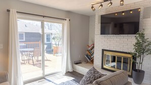 A living room with a fireplace, a sliding glass door to a patio, and a flat-screen TV mounted above the fireplace. - The Little Blue Inn (Rochester)