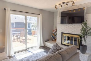 Ein Wohnzimmer mit Kamin, einer Schiebetür zu einer Terrasse und einem flachbildschirmfernseher, der über dem Kamin angebracht ist.