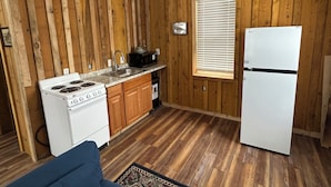 Cocina compacta con paneles de madera, estufa blanca, pileta, microondas y heladera.