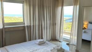 A hotel room with a bed, a window with curtains, a view of the outdoors, and a ceiling light. - Aegean Hill Skyview (Rafina)