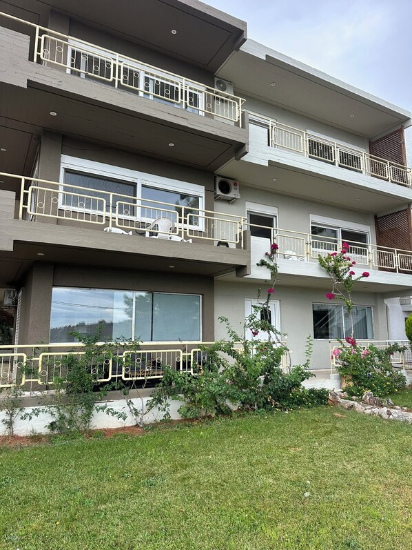 Un edificio residenziale a più piani con balconi, condizionatori d'aria e un piccolo giardino con piante e fiori.
