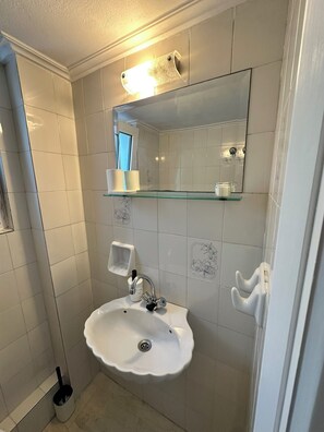 Un bagno con un lavandino bianco, uno specchio e un corpo illuminante sopra lo specchio.