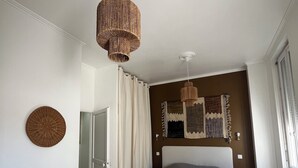 Un dormitorio con una cama grande, una lámpara colgante, un taburete pequeño y una ventana con cortinas.