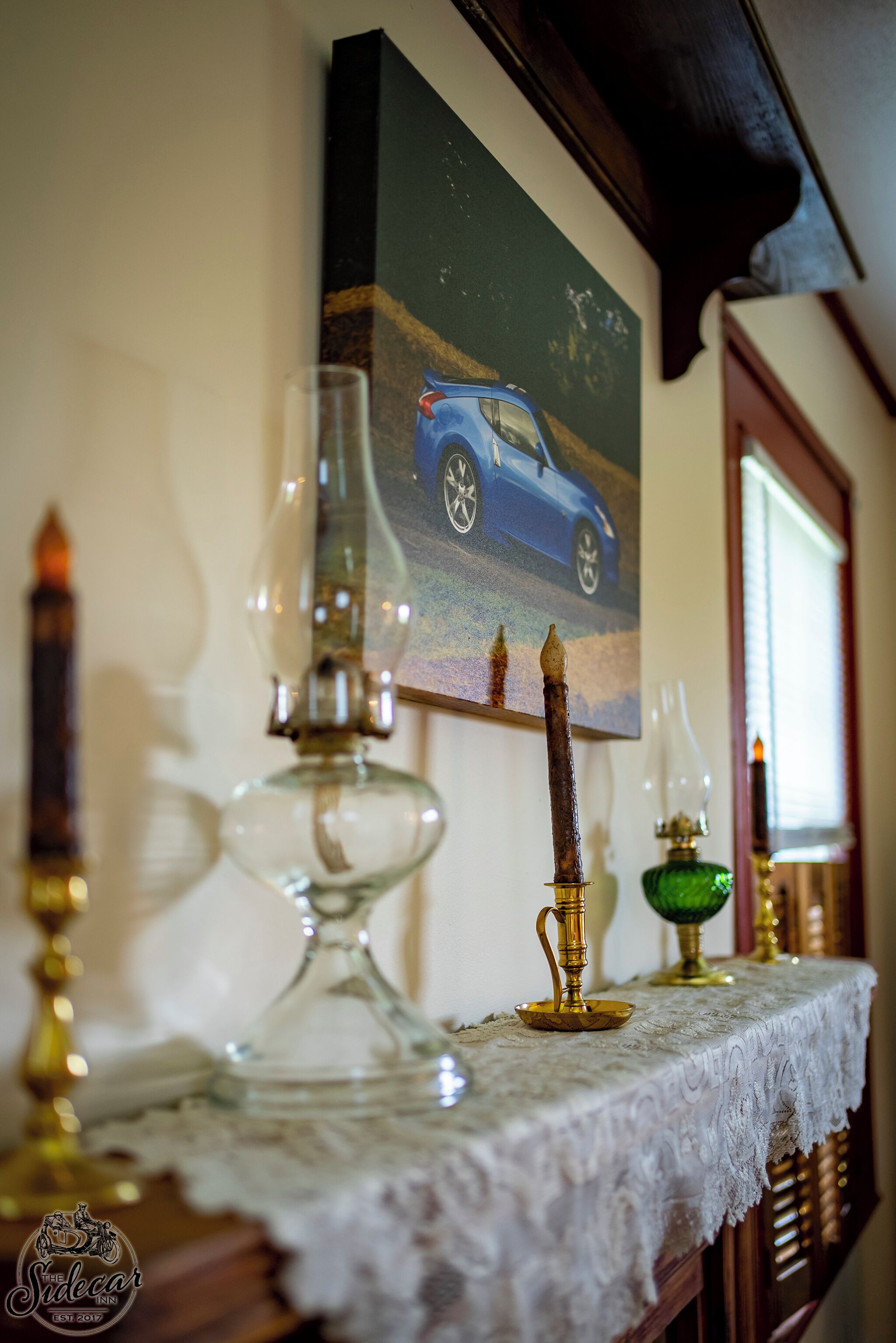 Ein Tisch mit einer Spitzenleinentischdecke, einem Auto-Gemälde und verschiedenen Dekoartikeln.