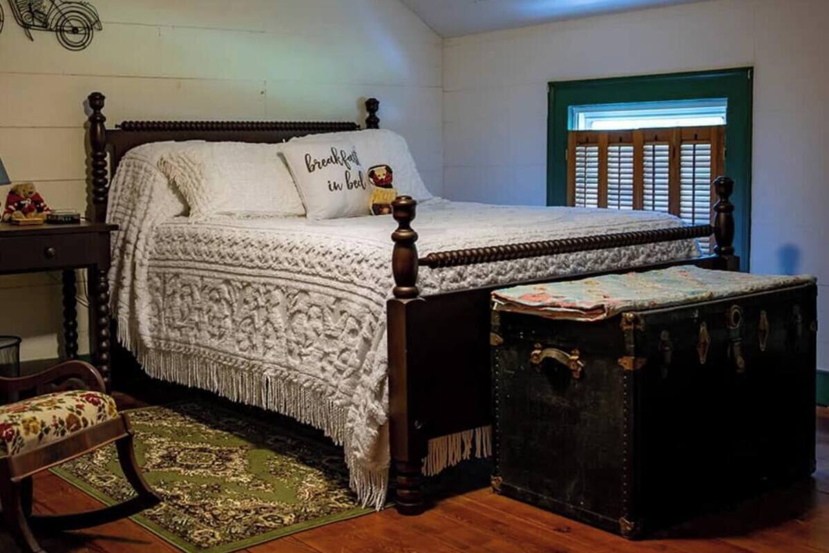 A bedroom with a four-poster bed, a vintage suitcase, and a green-framed window.