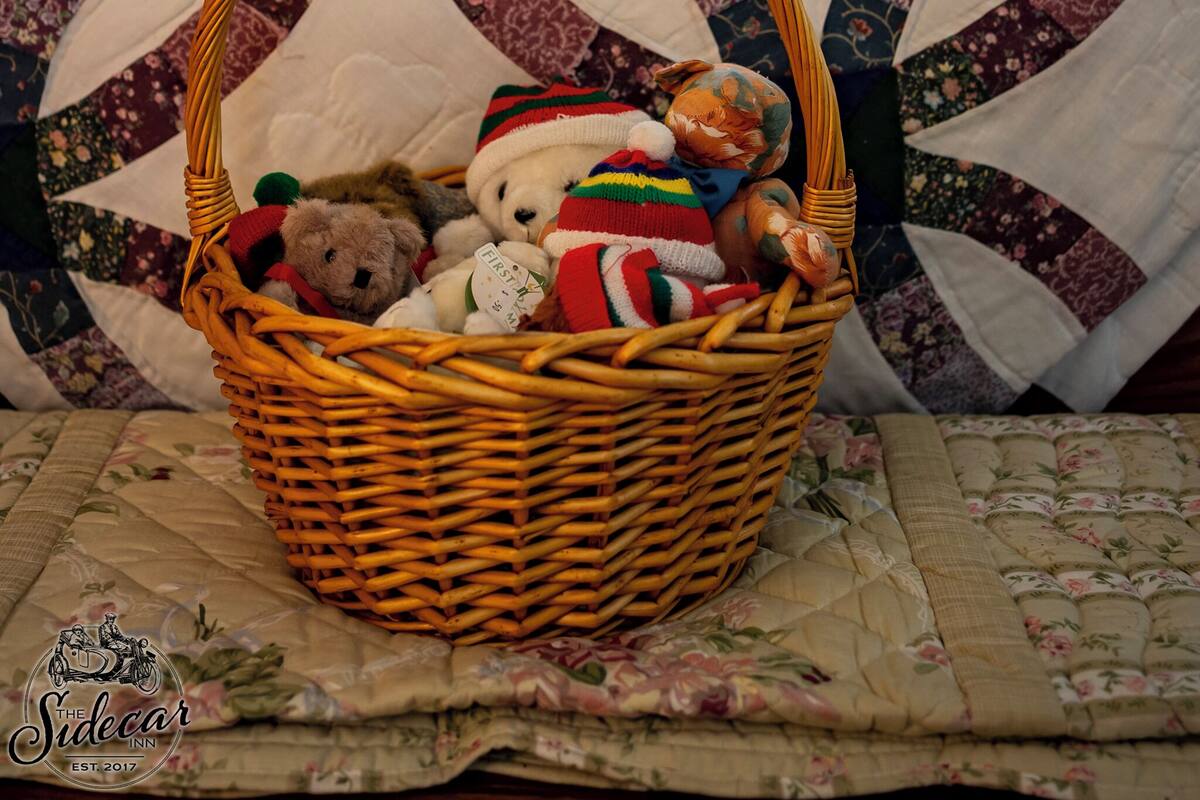 A bed with a quilt, a wicker basket with stuffed animals, and a window with blinds.